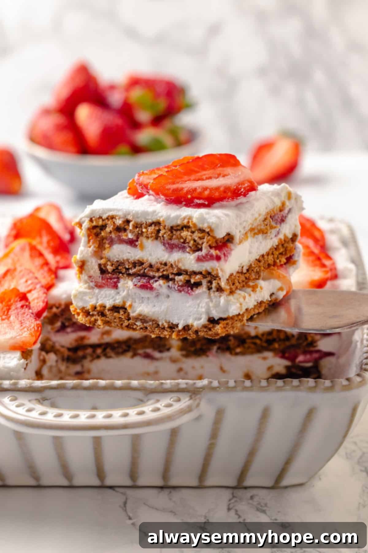 This strawberry icebox cake is cool, creamy, and super easy to make, with vegan whipped cream, fresh strawberries, and graham crackers. Yum! Lifting slice of strawberry icebox cake from dish