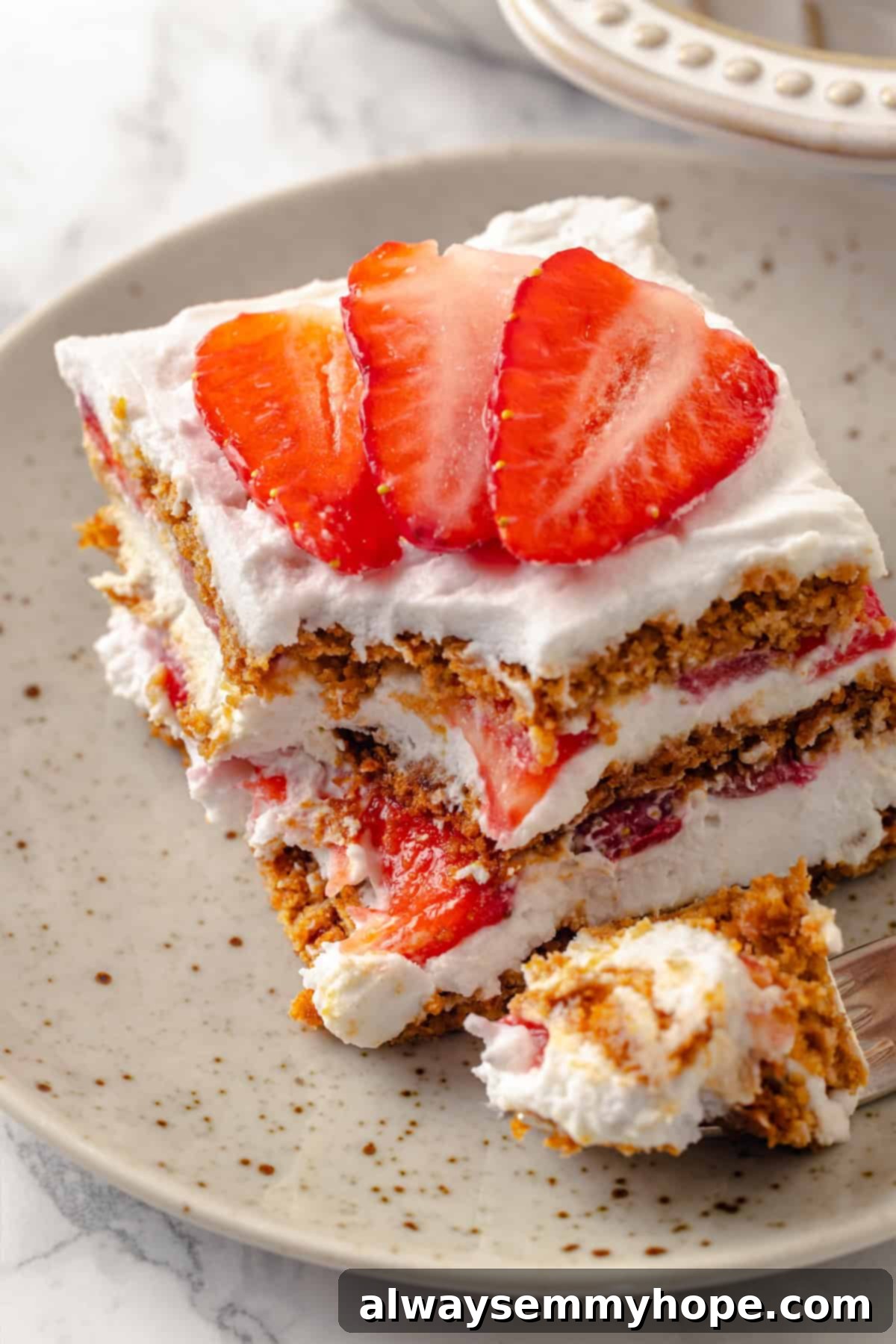 This strawberry icebox cake is cool, creamy, and super easy to make, with vegan whipped cream, fresh strawberries, and graham crackers. Yum! Slice of strawberry icebox cake on plate with corner on fork