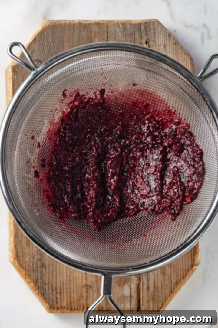 This summery blackberry margarita recipe is refreshing, delicious, and perfect for adding to your Taco Tuesday menu. It's always a hit! Overhead view of blackberry pulp being strained through a fine mesh sieve into a jar.
