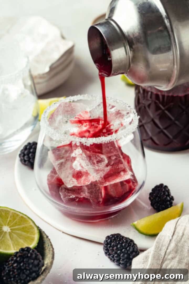 This summery blackberry margarita recipe is refreshing, delicious, and perfect for adding to your Taco Tuesday menu. It's always a hit! Pouring a vibrant blackberry margarita from a shaker into a glass with a salted rim and fresh ice.