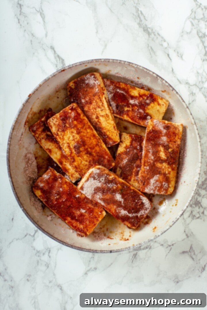 Crispy air fried tofu is layered with crunchy pickled veggies on crusty baguette to make this fresh and flavourful vegan Tofu Banh Mi recipe! Overhead view of tofu in bowl with soy sauce and seasonings being tossed