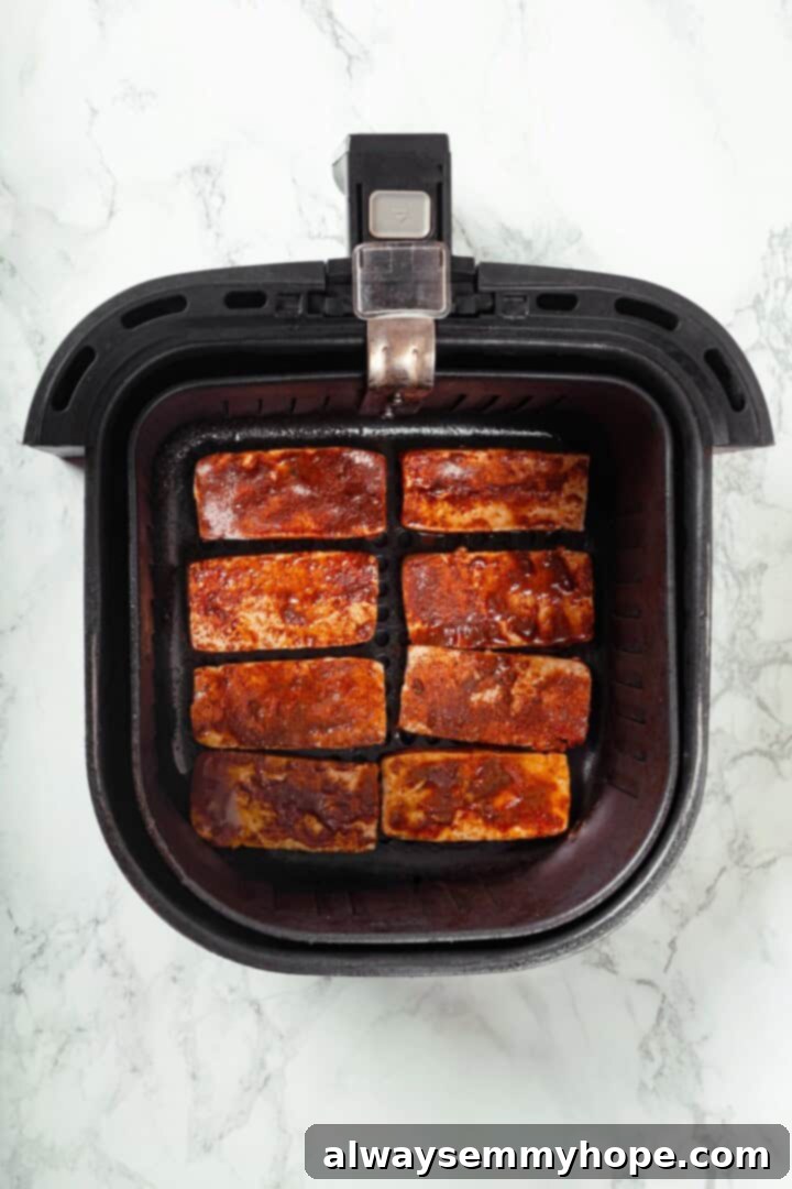 Crispy air fried tofu is layered with crunchy pickled veggies on crusty baguette to make this fresh and flavourful vegan Tofu Banh Mi recipe! Overhead view of seasoned tofu slices cooking in an air fryer basket until golden brown and crispy