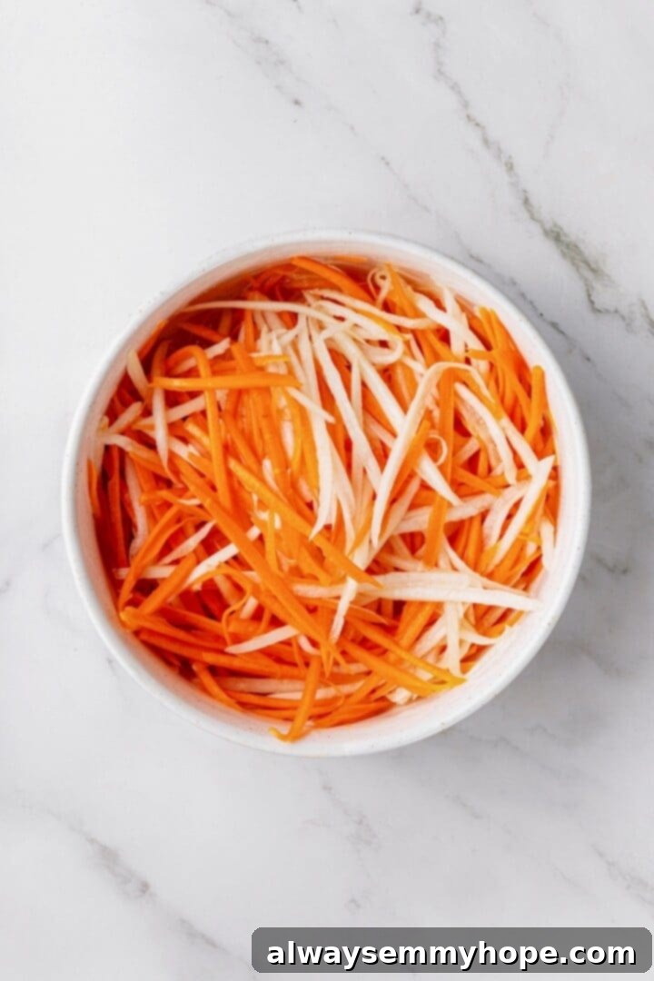 Crispy air fried tofu is layered with crunchy pickled veggies on crusty baguette to make this fresh and flavourful vegan Tofu Banh Mi recipe! Overhead view of julienned daikon radish and carrot marinating in pickling liquid in a bowl