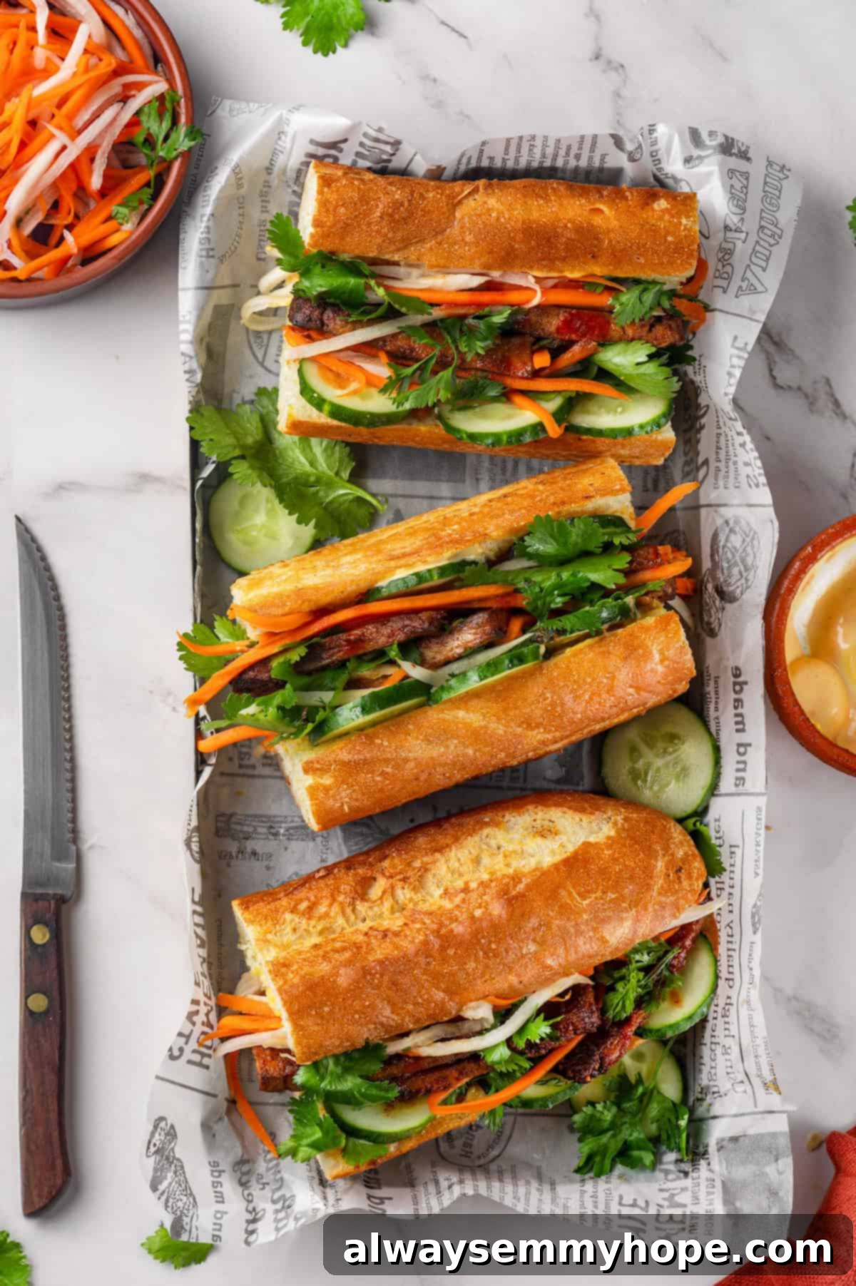 Crispy air fried tofu is layered with crunchy pickled veggies on crusty baguette to make this fresh and flavourful vegan Tofu Banh Mi recipe! Overhead view of three vegan tofu banh mi sandwiches artfully arranged in a wooden serving tray