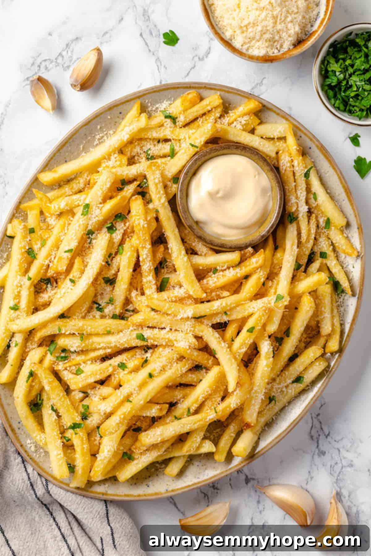 Whether you bake them or deep fry them, these crispy Garlic Fries are guaranteed to be a hit! They're cheesy, easy and packed with flavour. Overhead view of garlic fries on platter with bowl of aioli