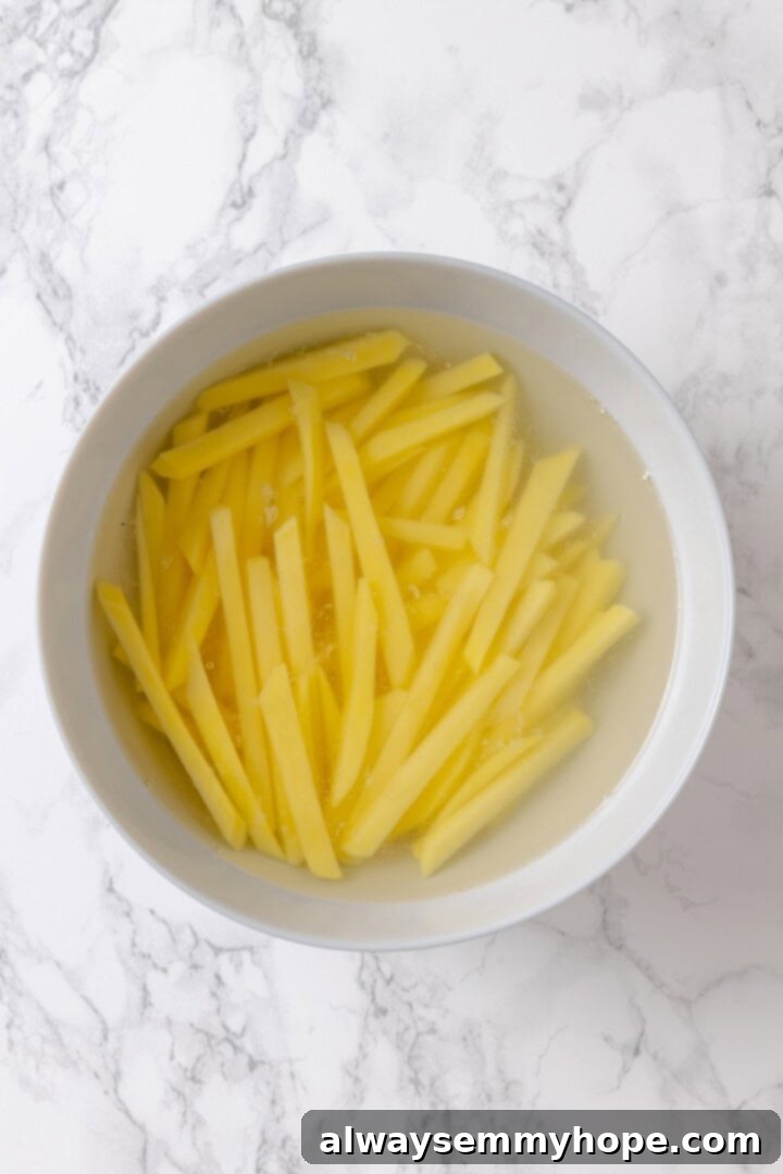Whether you bake them or deep fry them, these crispy Garlic Fries are guaranteed to be a hit! They're cheesy, easy and packed with flavour. Overhead view of fries soaking in bowl of cold water