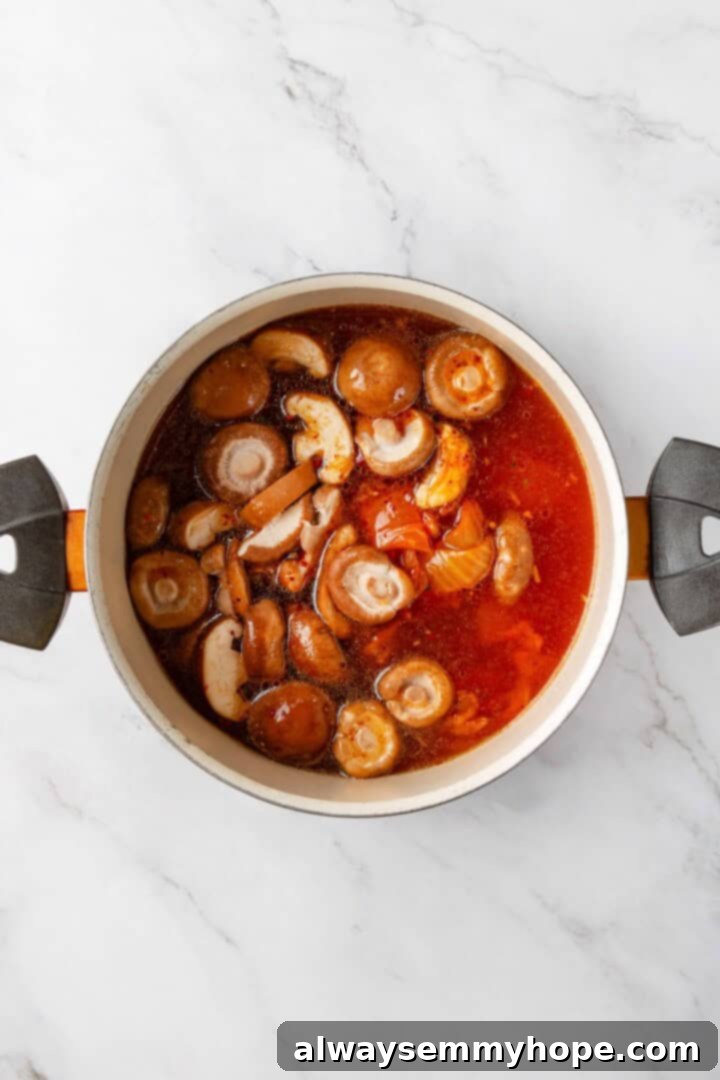 This spicy Kimchi Ramen is ridiculously easy, and the combination of tofu, kimchi, and shiitakes makes it a satisfying, flavour-packed meal! Sliced shiitake mushrooms being added to the simmering kimchi ramen broth, along with kimchi and spices, ready to absorb the rich flavors.