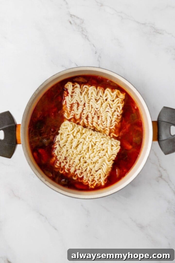 This spicy Kimchi Ramen is ridiculously easy, and the combination of tofu, kimchi, and shiitakes makes it a satisfying, flavour-packed meal! Instant ramen noodles being gently placed into the simmering kimchi broth, ready to cook until tender and absorb the delicious flavors.