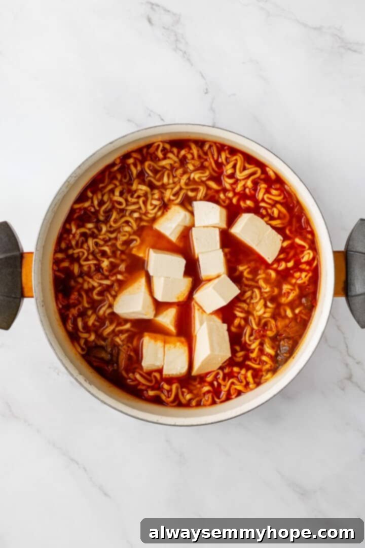 This spicy Kimchi Ramen is ridiculously easy, and the combination of tofu, kimchi, and shiitakes makes it a satisfying, flavour-packed meal! Crispy, golden-brown tofu cubes being stirred into the finished kimchi ramen, adding protein and texture before serving.