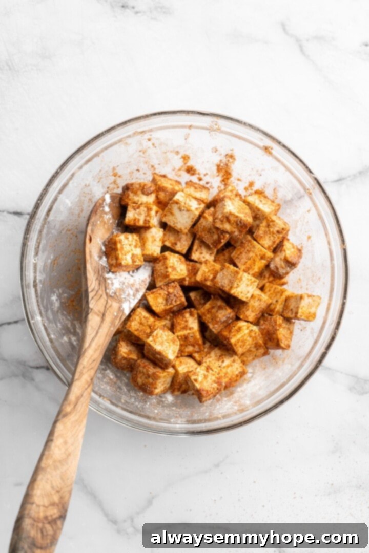 Seasoning Tofu for Air Frying Overhead view of tofu cubes mixed with a blend of garlic powder, onion powder, paprika, sea salt, cornstarch, soy sauce, sesame oil, and black pepper in a bowl, ready for air frying.