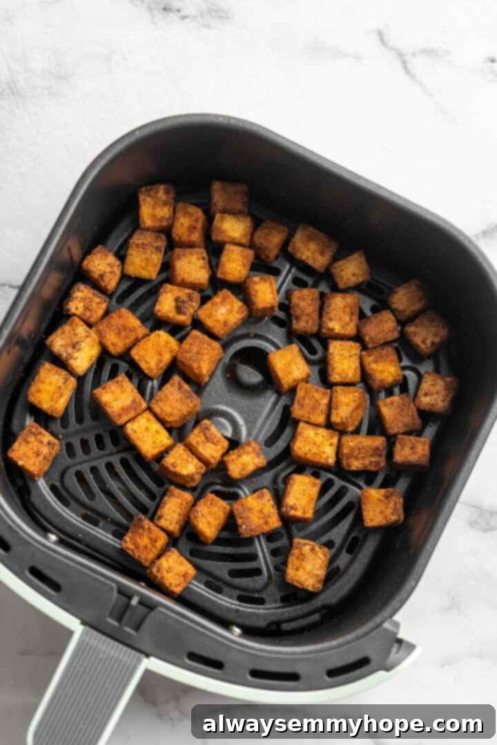 Air Frying Tofu to Crispy Perfection Overhead view of perfectly crispy, golden-brown tofu cubes arranged in a single layer within an air fryer basket, demonstrating the ideal texture achieved through air frying.