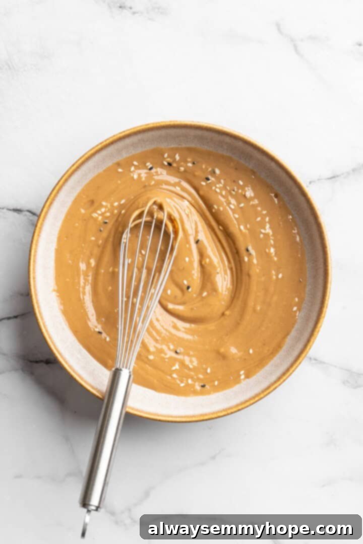 Making the Creamy Peanut Sauce Overhead view of a smooth, creamy peanut sauce being whisked in a bowl, showcasing its rich texture and vibrant color, ready to be drizzled over the tofu bowls.