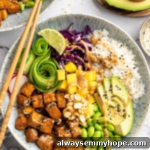 Peanut Tofu Meal Prep Bowls 2 Overhead view of a vibrant peanut tofu bowl, featuring golden crispy tofu, fresh mango, bright green edamame, creamy avocado, and fluffy rice, all generously drizzled with a rich peanut sauce.