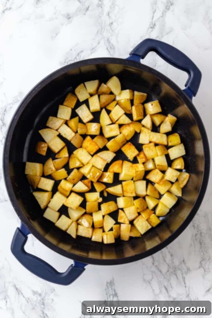 Overhead view of diced Yukon Gold potatoes cooking in a large skillet, lightly browned