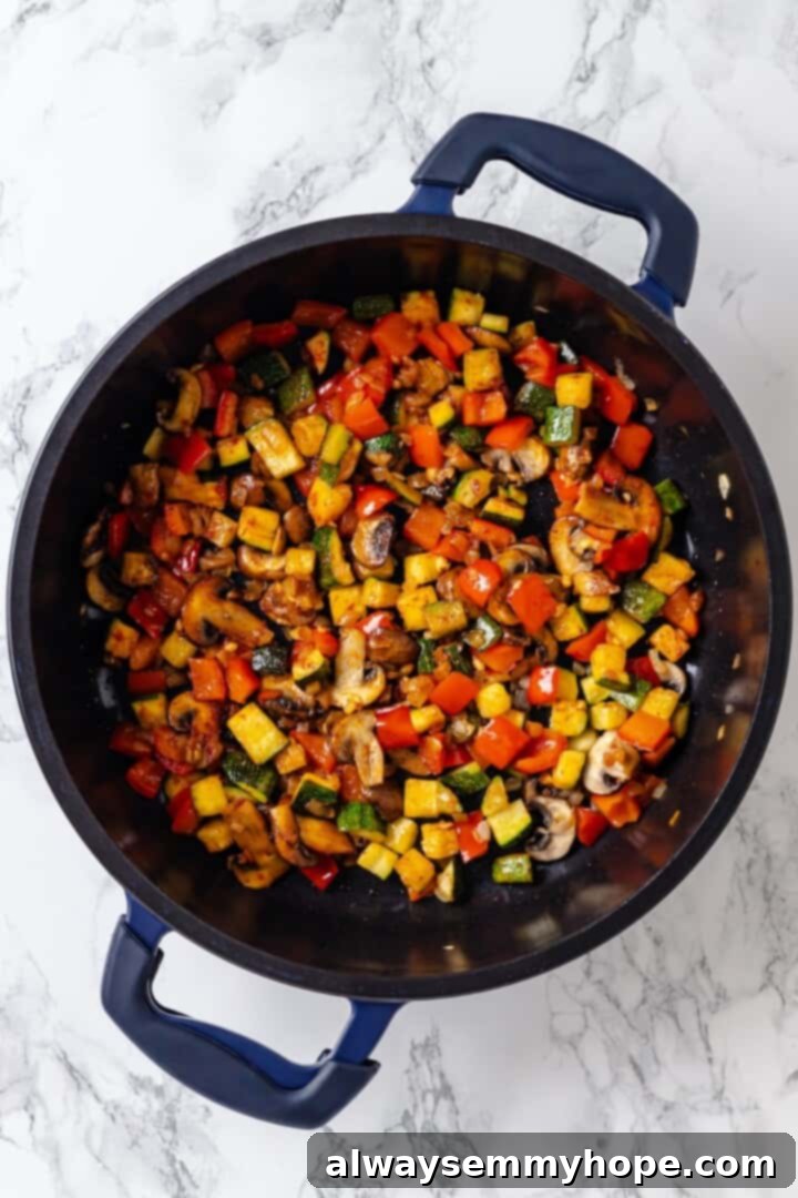 Overhead view of bell pepper, zucchini, and mushrooms cooking in a cast iron skillet with onions
