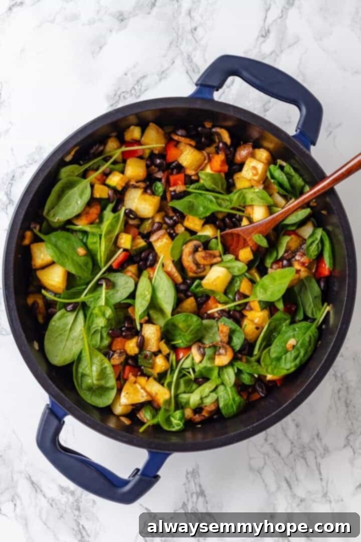 Overhead view of baby spinach being added to the skillet with cooked hash ingredients