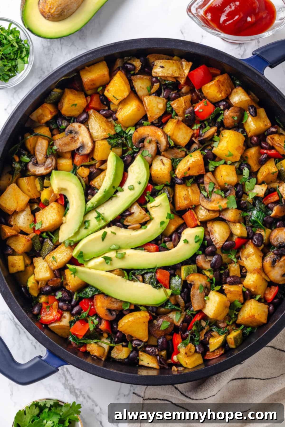 Overhead view of vegan breakfast hash in a cast iron skillet, topped with fresh avocado slices and cilantro