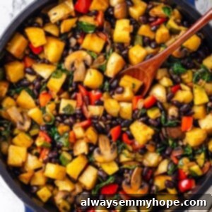 Skillet of vegan breakfast hash with wooden spoon, showcasing the rich colors of vegetables and potatoes