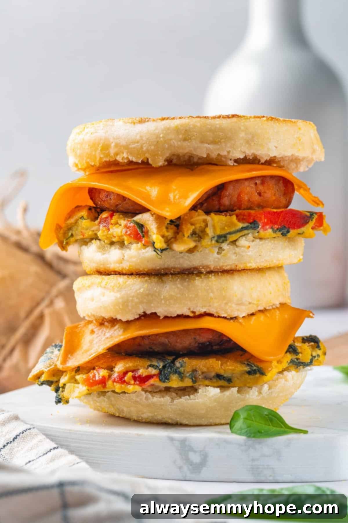 Two beautifully stacked vegan breakfast sandwiches on a sleek marble board, showcasing the fluffy omelet, savory sausage, and melted cheddar