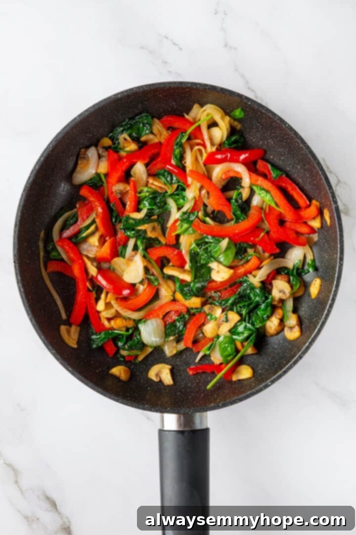 Overhead view of colorful vegetables, including mushrooms, bell pepper, onion, and spinach, cooked in a skillet