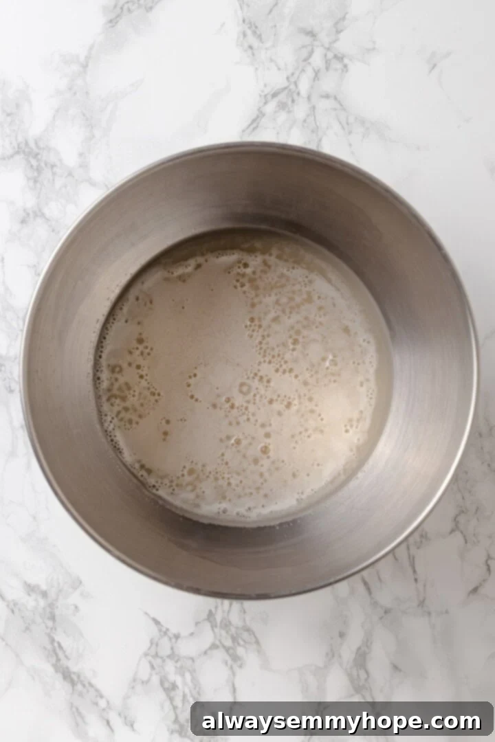 Activate the yeast in warm water and sugar to ensure a good rise for your French bread dough. Overhead view of a mixing bowl containing warm water, sugar, and instant yeast, showing the foamy activation process.