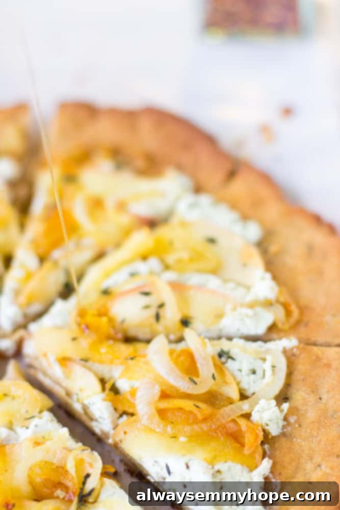 This Goat Cheese Pizza with Caramelized Onions and Apples is sprinkled with thyme, drizzled with honey and incredibly tasty! Close-up, top-down shot of a freshly baked goat cheese and apple pizza, showing individual slices and the vibrant toppings.