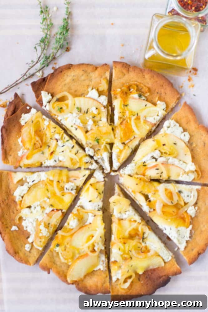 This Goat Cheese Pizza with Caramelized Onions and Apples is sprinkled with thyme, drizzled with honey and incredibly tasty! Overhead shot of a full goat cheese pizza alongside a small dish of olive oil, ready to be served and enjoyed.