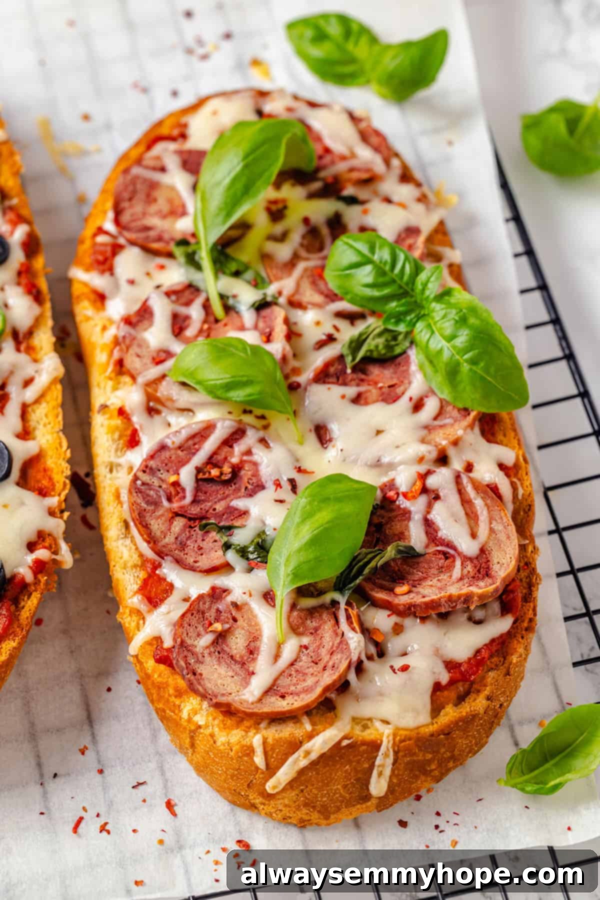 This vegan French Bread Pizza recipe is cheesy, easy and that thick, toasty base puts regular crust to shame. I’ve got two topping options! Fresh basil leaves scattered over vegan French bread pizza topped with salami and melted cheese
