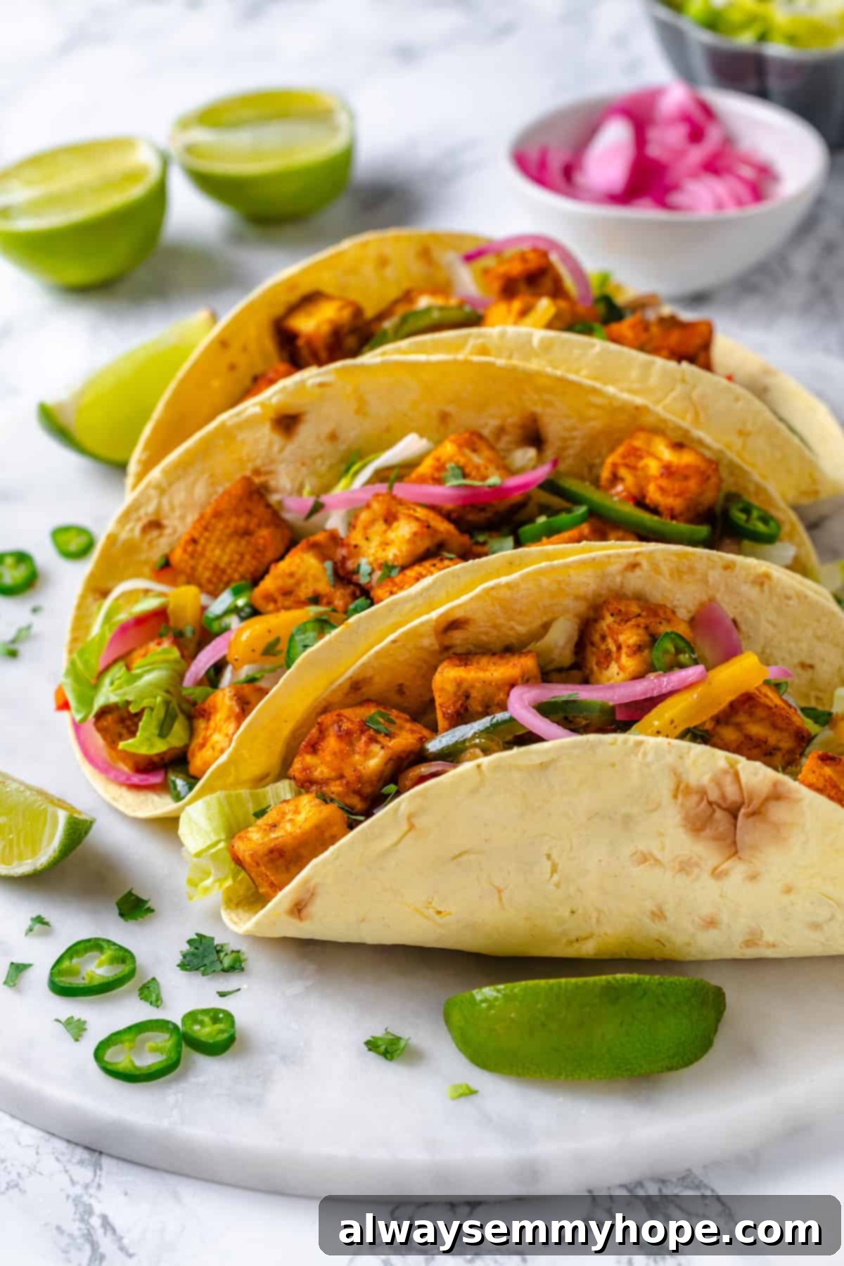 Three beautifully arranged crispy tofu tacos topped with fajita mushrooms and fresh veggies, served on a stylish marble tray.