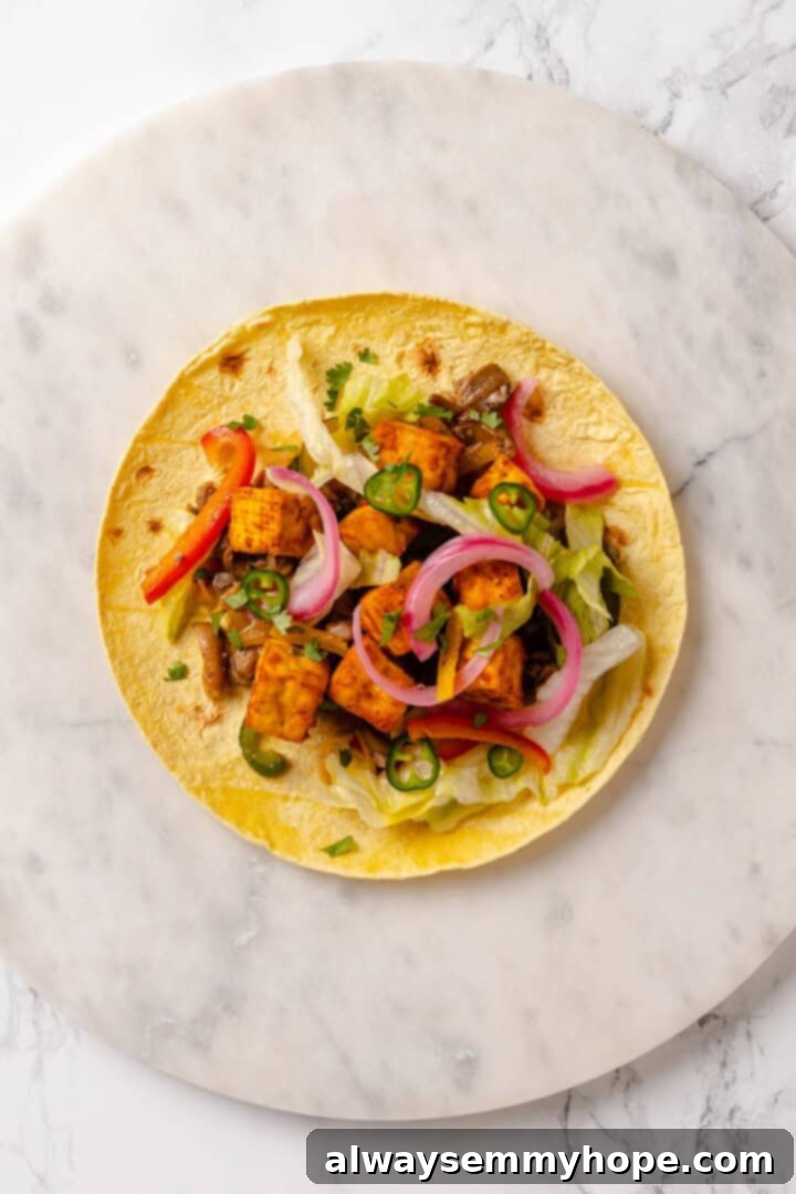 A close-up overhead view of a finished tofu taco, layered with crispy tofu, fajita vegetables, and vibrant pickled red onions.