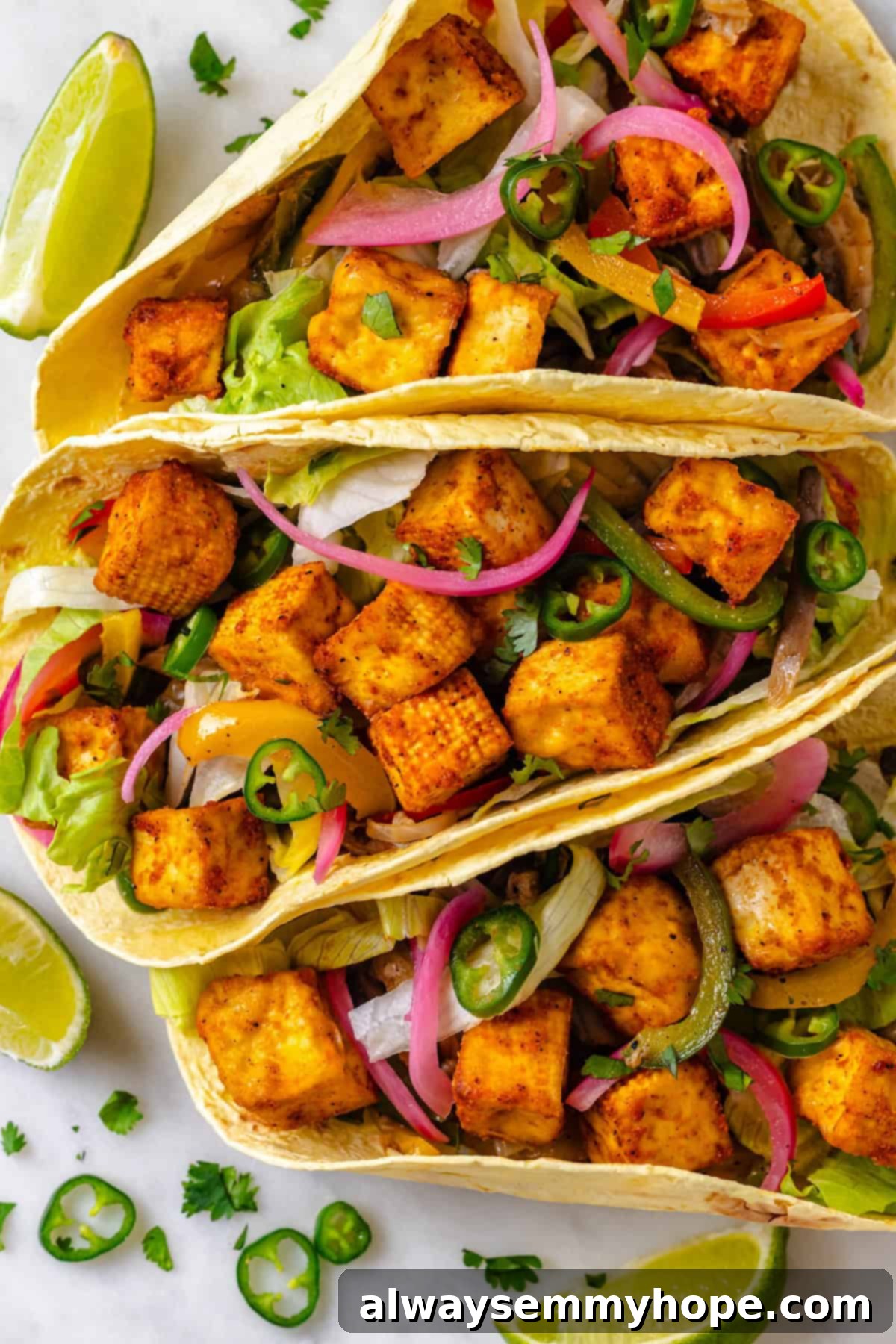 An inviting overhead view of three fully assembled vegan tofu tacos, brimming with crispy tofu and colorful fajita vegetables, ready to be enjoyed.