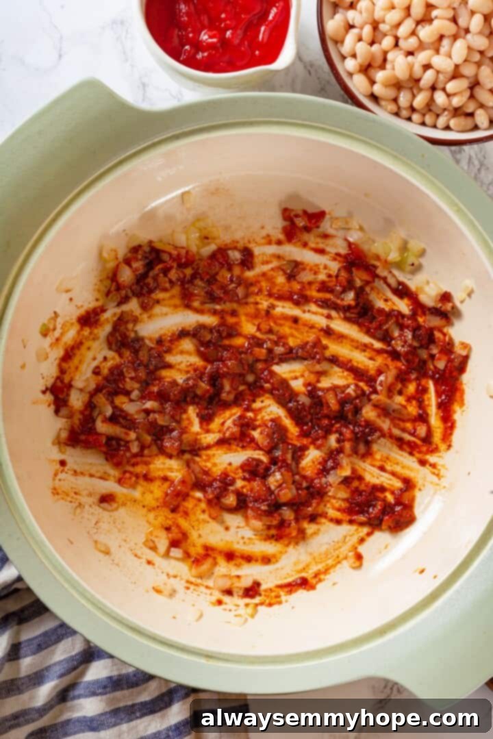 This vegan Baked Beans recipe has all the sweet, tangy, smoky flavour you love! Starting with canned beans makes this recipe a cinch. Overhead view of tomato paste cooking in pot