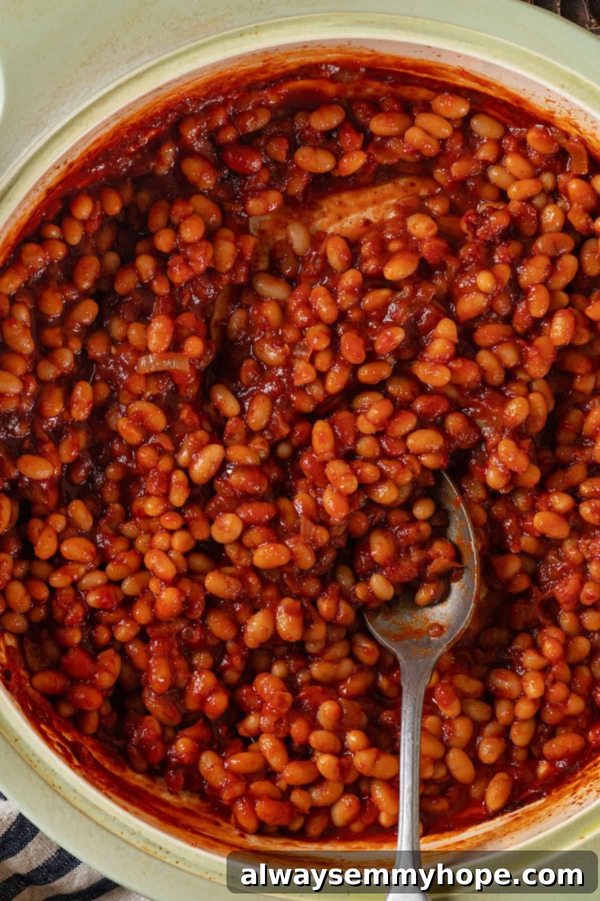 This vegan Baked Beans recipe has all the sweet, tangy, smoky flavour you love! Starting with canned beans makes this recipe a cinch. Overhead view of vegan baked beans in pot with spoon