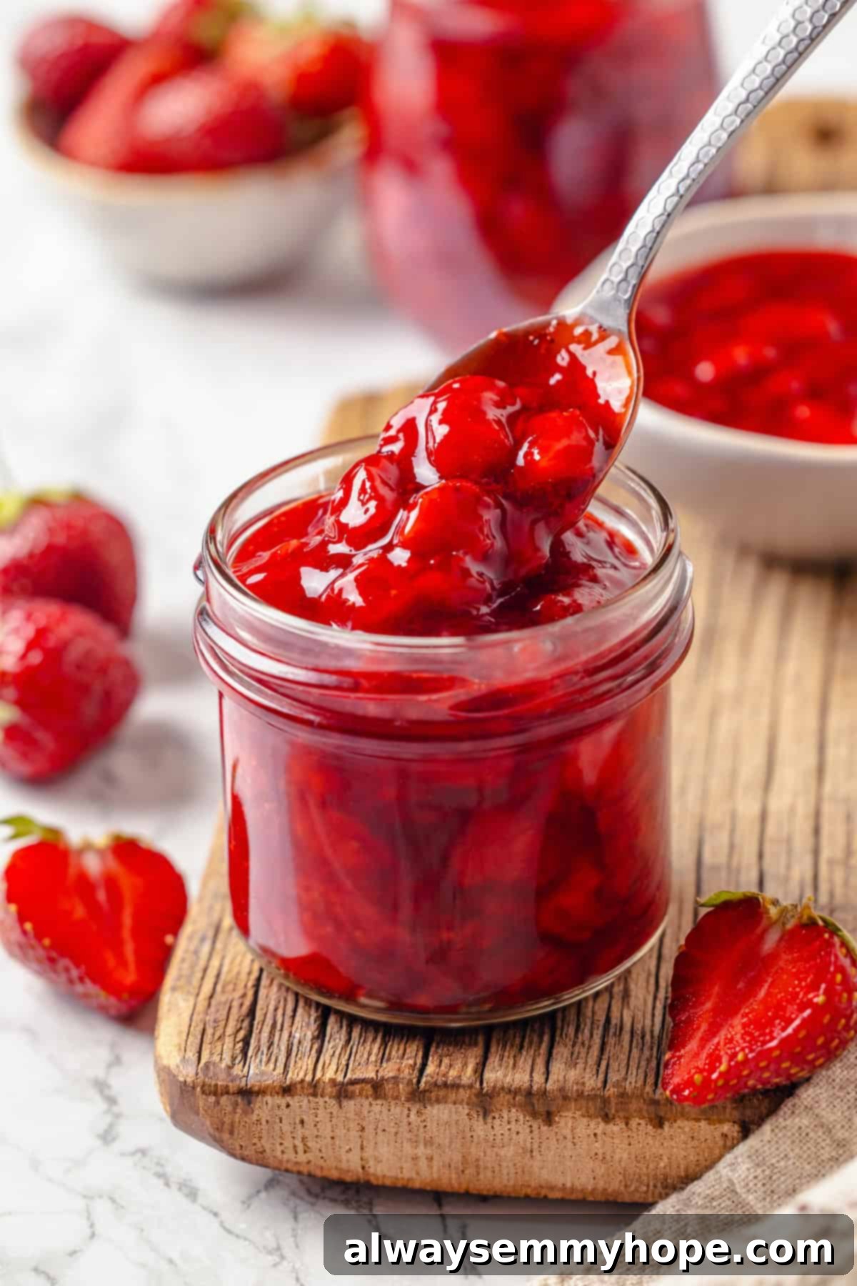 Spoonful of vibrant red homemade strawberry cake filling held over a glass jar