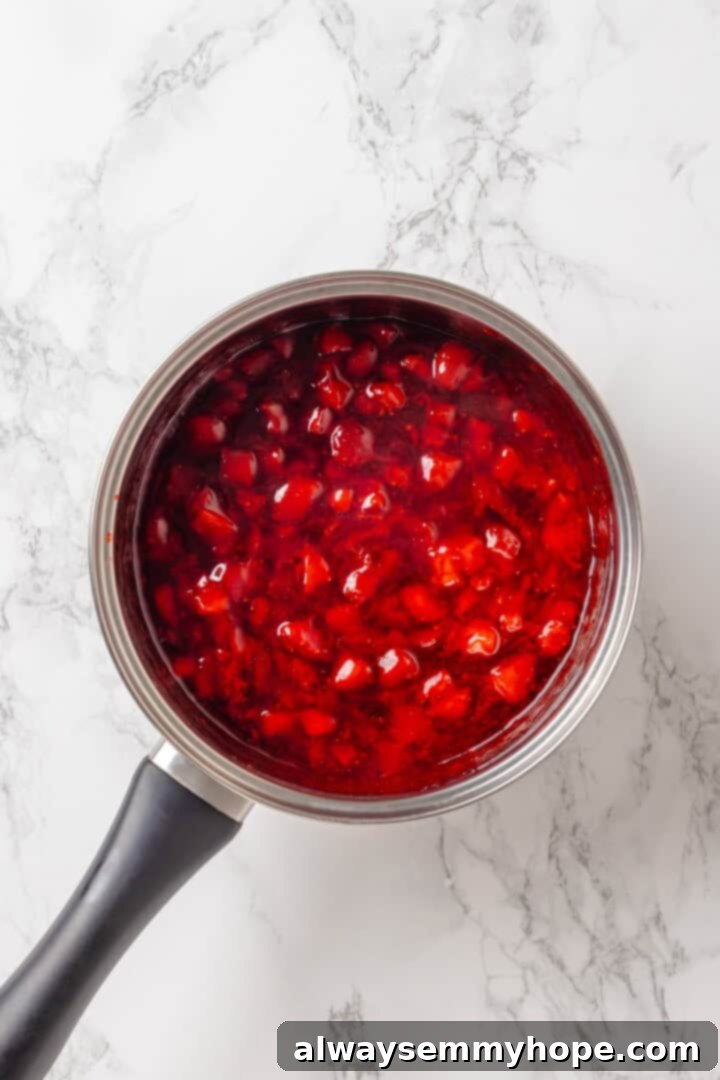 Overhead view of strawberry cake filling thickening in a saucepan after adding cornstarch slurry