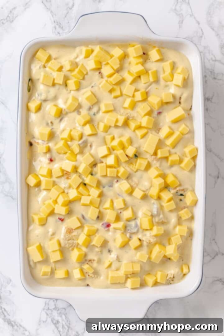 An overhead view of the vegan overnight breakfast strata assembled in a baking dish, before being chilled and baked, topped with vegan cheese.