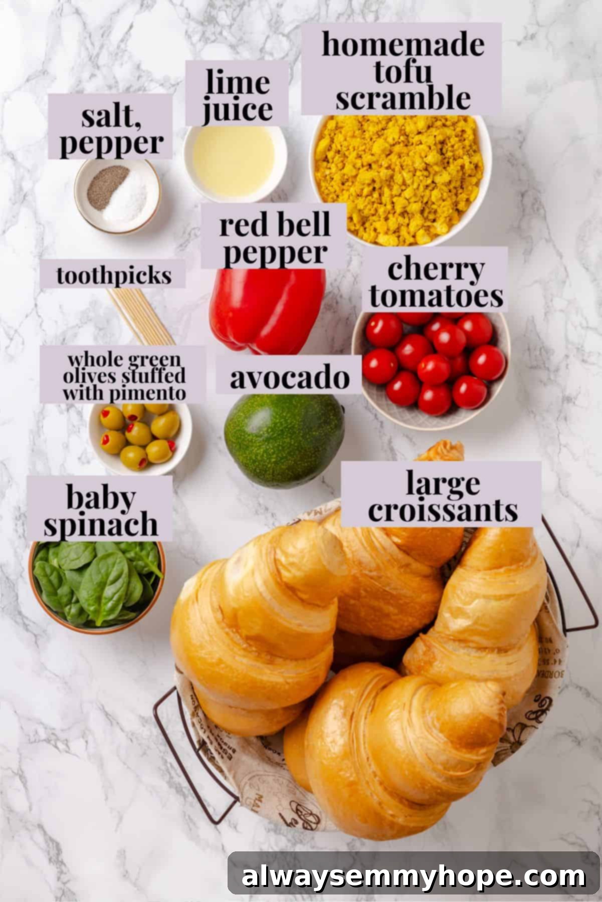 Fresh ingredients like vegan croissants, avocado, red pepper, spinach, and tofu scramble for Monster Breakfast Sandwiches. Overhead view of fresh ingredients for monster breakfast sandwich on a white surface