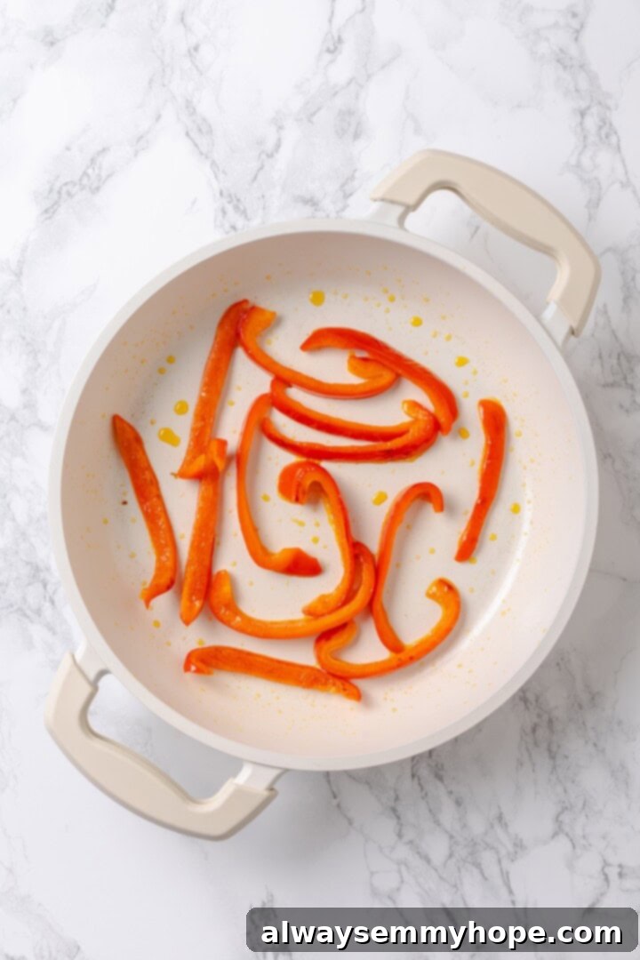 Overhead view of bright red bell pepper strips softening in a skillet