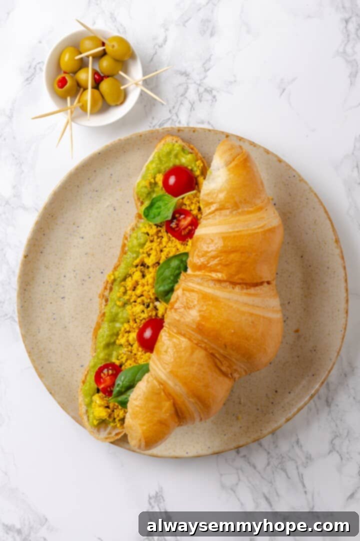 Overhead view of a vegan monster breakfast sandwich being assembled with avocado, tofu scramble, and vegetables