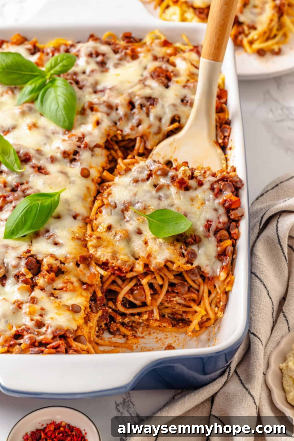 A spatula lifts a generous portion of cheesy, layered vegan Million Dollar Spaghetti from a deep baking dish, showcasing its rich texture and enticing layers.