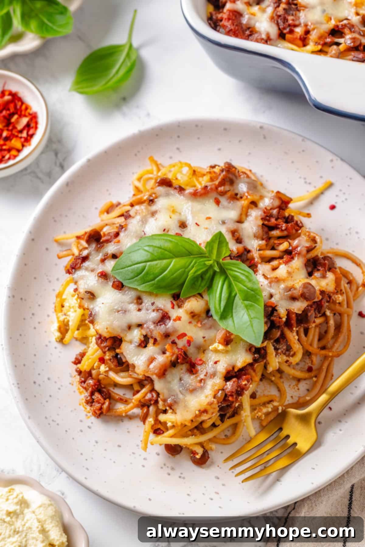 A close-up shot of a perfect slice of vegan Million Dollar Spaghetti on a white plate, with a fork ready to scoop, highlighting the layers and melted cheese.