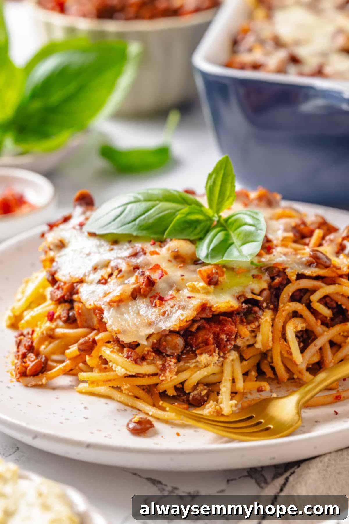 A close-up of a serving of vegan Million Dollar Spaghetti on a plate, with a fork extracting a creamy, saucy bite, showing the delicious layers.
