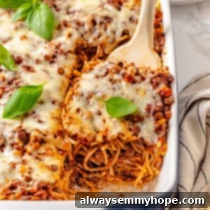 A spatula lifting a generous portion of cheesy, layered vegan Million Dollar Spaghetti from a deep baking dish, showcasing its rich texture and enticing layers.