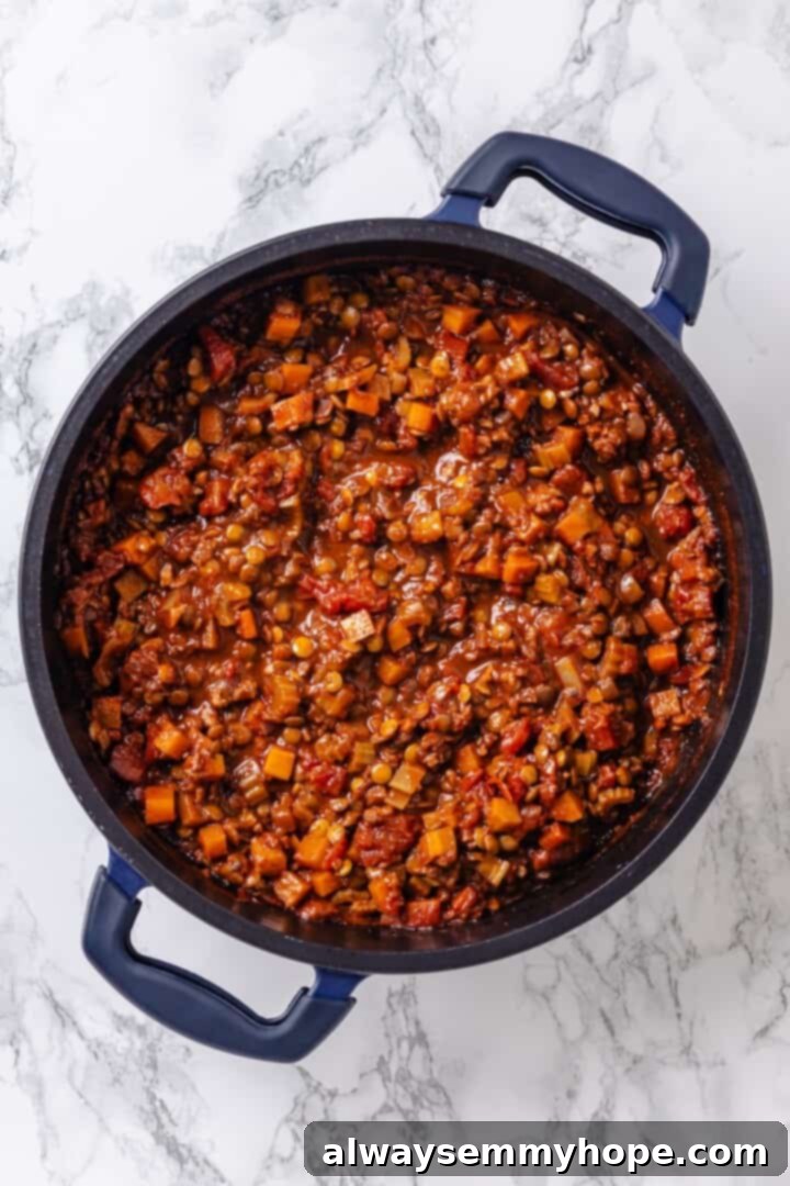 The simmering vegan bolognese sauce in a pot, now enriched with lentils, vegetable broth, crushed tomatoes, and a touch of sugar.