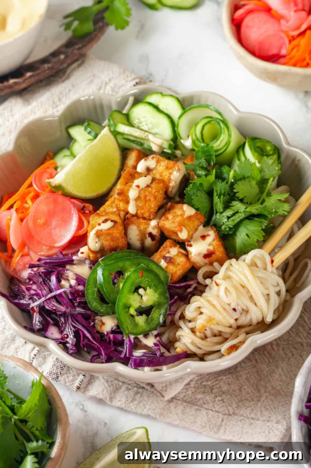 A vibrant vegan banh mi bowl featuring chewy rice noodles, crispy tofu, and colorful fresh vegetables, with chopsticks ready for serving.