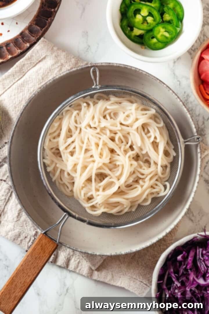 Drained rice noodles resting in a colander over a pot, ready for assembly.