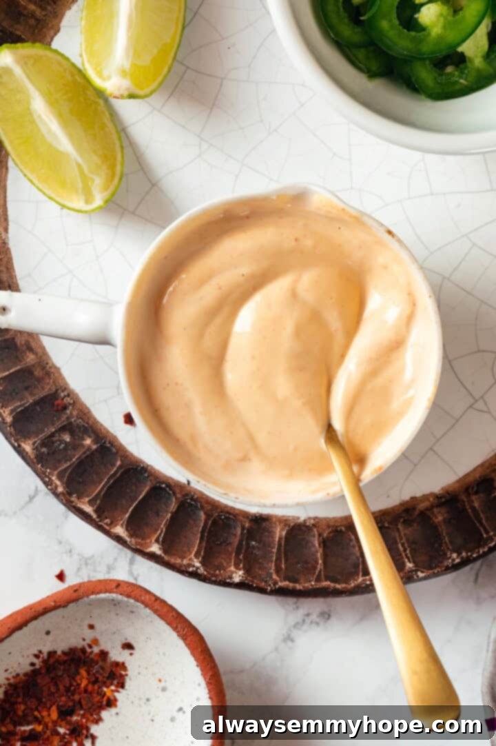 Creamy sriracha mayo mixture in a measuring cup with a spoon, ready to be drizzled.