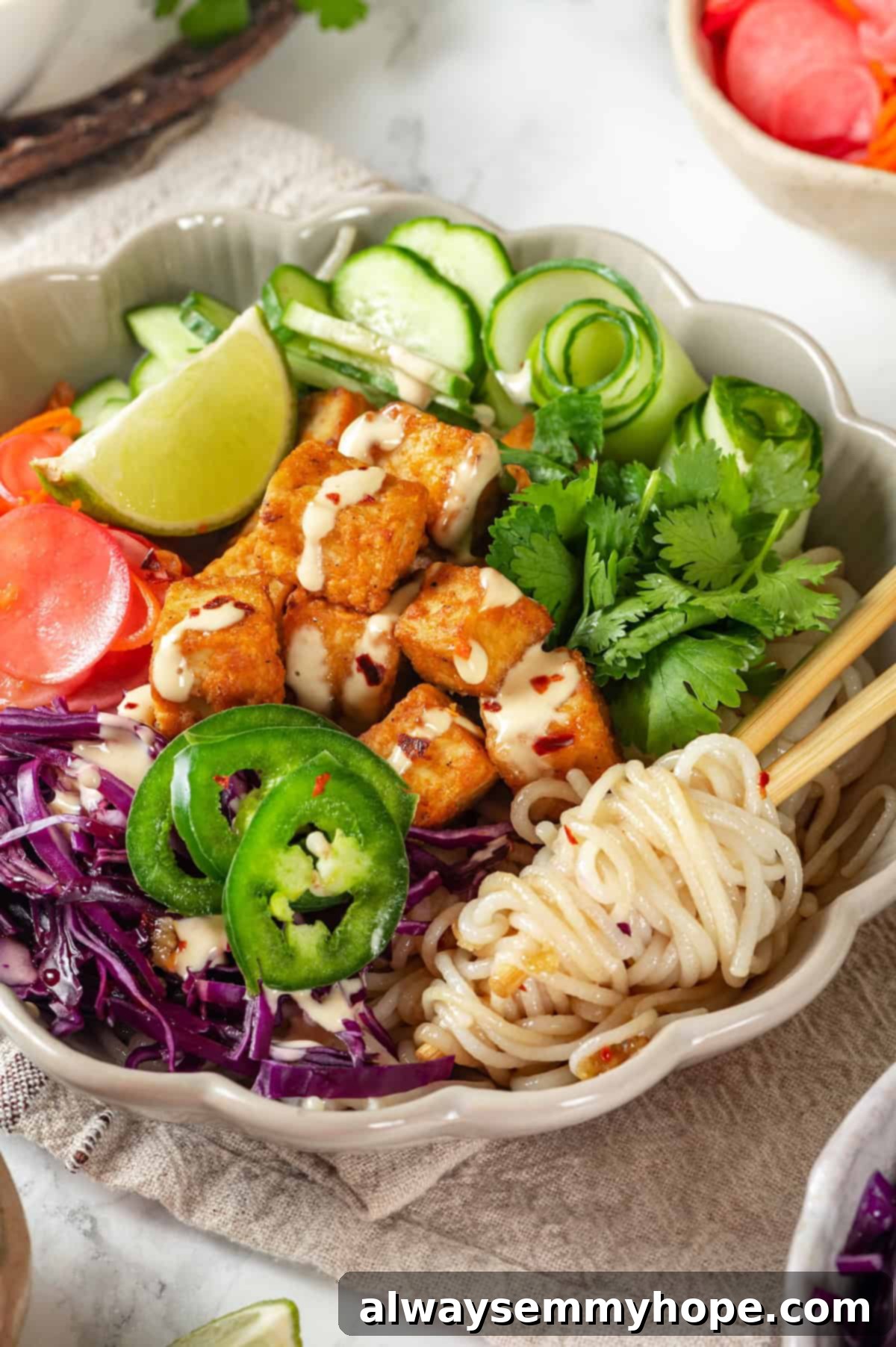 Close-up of rice noodles perfectly twirled around chopsticks, ready to be eaten from a vibrant vegan banh mi bowl.