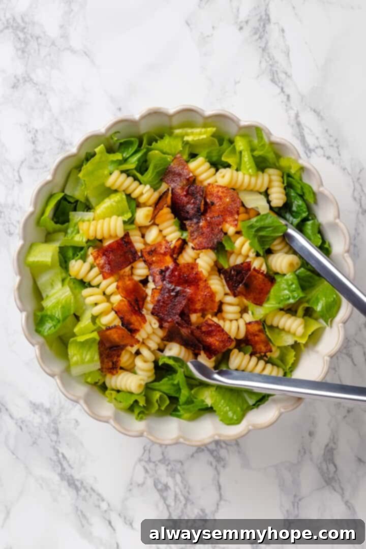 This vegan Caesar Pasta Salad is savoury, tangy and garlicky, with crunchy baked chickpeas, crisp romaine and tender pasta. Delicious! Tongs tossing ingredients for caesar pasta salad.