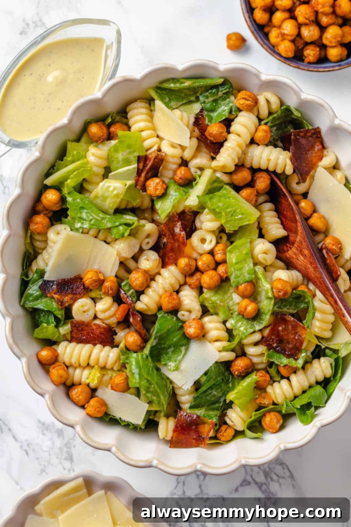 This vegan Caesar Pasta Salad is savoury, tangy and garlicky, with crunchy baked chickpeas, crisp romaine and tender pasta. Delicious! Bowl of caesar pasta salad with wooden spoon.